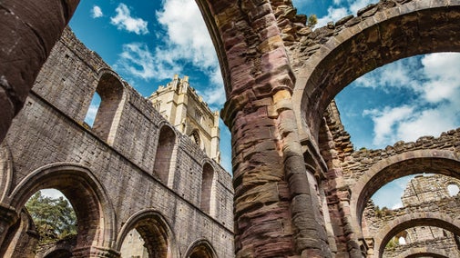 Blue skies shine through the missing roof in the nave of Fountains Abbey as Huby's Tower looms over